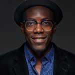 The portrait of handsome young black african smiling man in hat on dark background. Positive human emotions